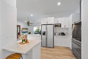 Una cocina moderna con armarios blancos, un refrigerador de acero inoxidable, una estufa y piso de madera.