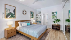 Une chambre à coucher avec un lit, des tables de chevet, un ventilateur de plafond et un grand miroir.