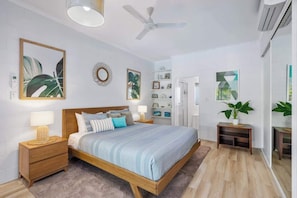 Un dormitorio con cama, mesitas de noche, ventilador de techo y un espejo grande.