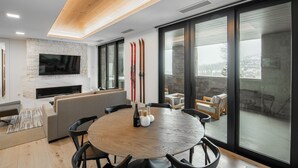 Ein modernes Wohnzimmer mit Kamin aus Stein, einem Flachbildfernseher, einem runden Holztisch mit Stühlen und einem Balkon mit Sitzgelegenheit.