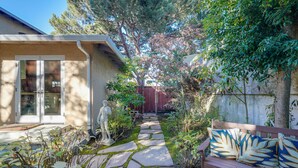 A stone pathway leading to a wooden bench with cushions, surrounded by greenery and a statue. - Seascape Aptos Retreat w/ Bocce Ball Court! (Aptos)