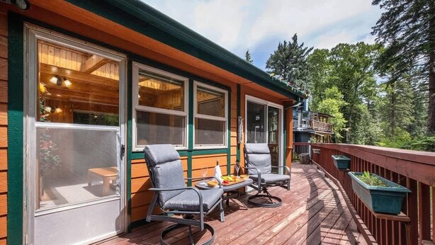 A wooden deck with two chairs and a table, overlooking a forested area.