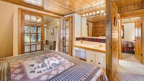 A cozy bedroom with a wooden ceiling, a large bed with a patterned quilt, a bedside table, and a mirror above it.