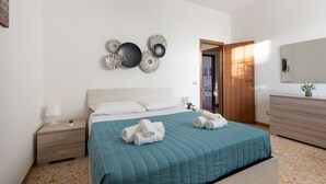 Un dormitorio con una cama, mesitas de noche, una obra de arte en la pared, una puerta de madera y un espejo.
