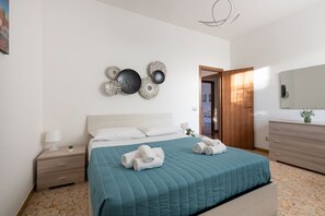 A bedroom with a bed, bedside tables, a wall-mounted artwork, a wooden door, and a mirror.
