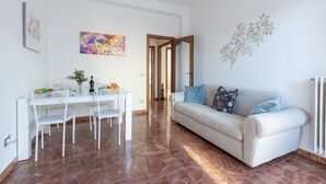 Un comedor con una mesa y sillas blancas, un sofá con cojines azules y un cuadro en la pared.