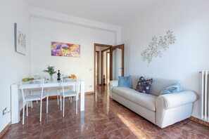 A dining area with a white table and chairs, a sofa with blue cushions, and a painting on the wall.