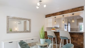 Una cocina moderna con una pared de acento de piedra, un área de comedor con mesa de vidrio y sillas color turquesa, y un mueble bajo blanco con cajones.