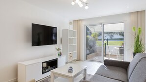 Una sala de estar moderna con un televisor de pantalla plana, un mueble blanco para entretenimiento, un sofá gris, una mesa de centro y un puerta corrediza de vidrio que da a un patio al aire libre.