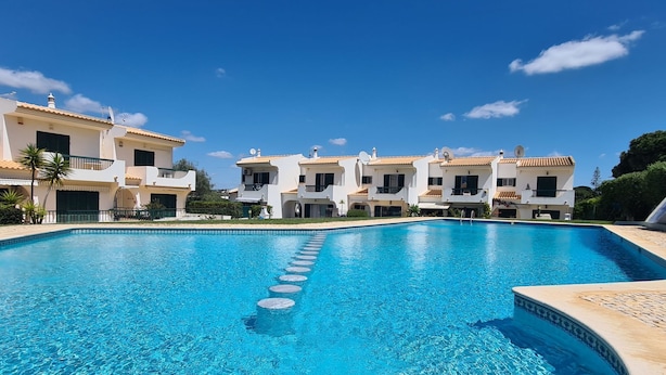 Una piscina con agua cristalina azul, rodeada de edificios blancos con balcones y antenas parabólicas.