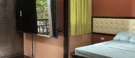 Une chambre d’hôtel avec un lit, un téléviseur fixé au mur, un miroir et une fenêtre donnant sur un paysage verdoyant.