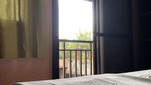 A room with a bed, a window with a view of greenery, and a door leading outside. - Alona Princess Suites (Panglao)
