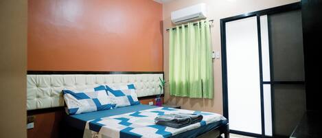 A bedroom with a bed, a window with green curtains, an air conditioning unit, and a sliding door.