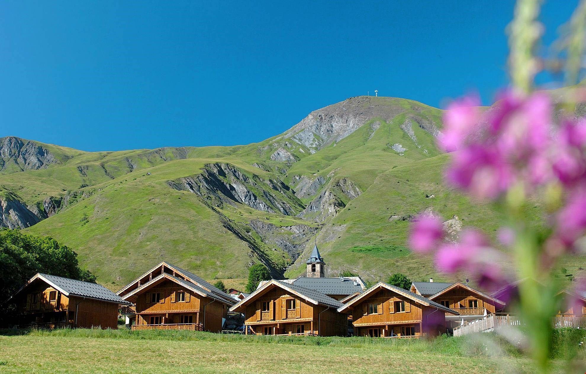 Une rangée de cabanes en bois, avec une vue sur les montagnes et le clocher d’une église en arrière-plan.