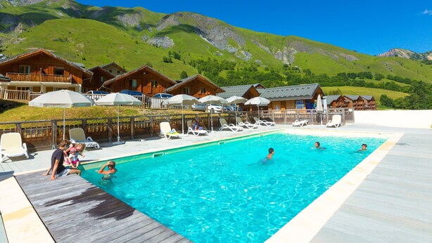 Un espace piscine agrémenté de cabanes en bois, avec une chaîne de montagnes en toile de fond.