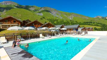 Un espace piscine agrémenté de cabanes en bois, avec une chaîne de montagnes en toile de fond.