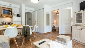 Une cuisine moderne équipée d’un four à micro-ondes, d’un réfrigérateur et d’une machine à café. Un coin repas avec une table et des chaises est à disposition, ainsi qu’un salon avec un canapé et un téléviseur.
