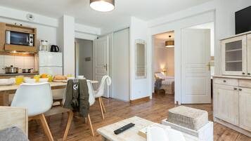 Une cuisine moderne équipée d’un four à micro-ondes, d’un réfrigérateur et d’une machine à café. Un coin repas avec une table et des chaises est à disposition, ainsi qu’un salon avec un canapé et un téléviseur.
