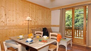 Une pièce aux murs lambrissés, avec une table à manger dressée pour le petit-déjeuner, un banc et une vue sur la verdure par une porte vitrée.