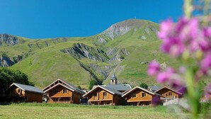 Une rangée de cabanes en bois, avec une vue sur les montagnes et le clocher d’une église en arrière-plan.