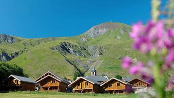 Une rangée de cabanes en bois, avec une vue sur les montagnes et le clocher d’une église en arrière-plan.
