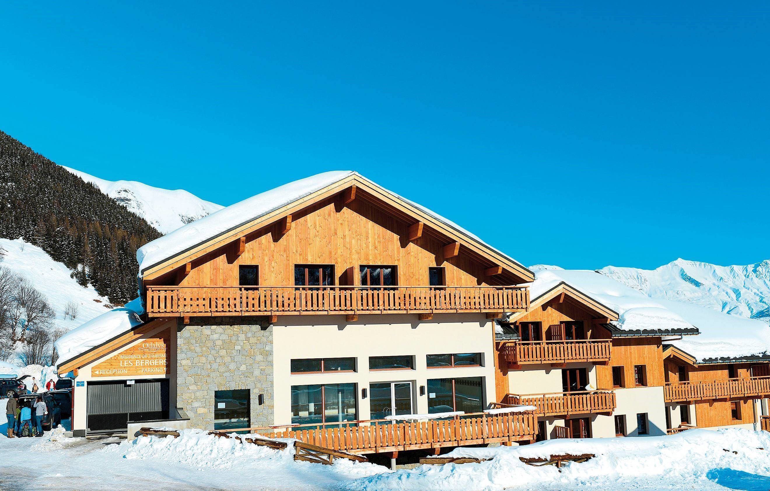 Un chalet en bois doté d’un espace d’accueil et d’un parking, entouré de neige et de montagnes.