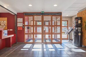 Entrada de hotel com porta giratória, balcão de recepção e máquina de venda automática.