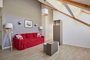 Uma sala de estar moderna com um sofá vermelho, duas luminárias de chão, um quadro na parede e uma escada.