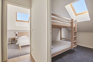 Quarto em dormitório com beliches, claraboia, mesa de cabeceira e luminária.