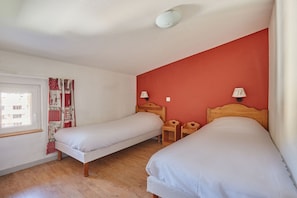 A room with two single beds, wooden nightstands, a red wall, and a window with curtains.