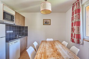 Eine kleine Küche mit Mikrowelle, Herd und Spüle. Ein Esstisch mit Stühlen und eine Hängelampe sind vorhanden. Ein gerahmtes Bild hängt an der Wand.