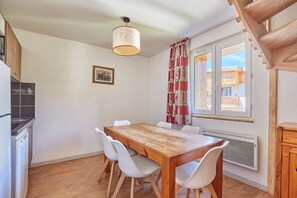 Un comedor con mesa de madera y sillas blancas, una ventana con vistas, y una cocina con estufa.