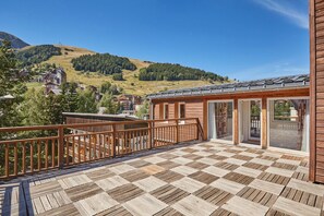 Una terraza de madera con piso a cuadros, baranda de madera y vista a un paisaje montañoso.