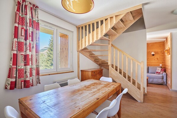 A room with a wooden staircase, a dining table with chairs, and a view of the outdoors through a window.