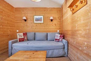 A wooden cabin interior with a grey sofa, two wall-mounted lamps, and a framed picture above the sofa.