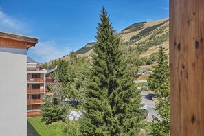 Ein Hotel mit Balkon, einem großen immergrünen Baum und Blick auf eine hügelige Landschaft.