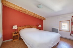 A bedroom with a wooden headboard, a single bed, two bedside lamps, a window with curtains, and a radiator.