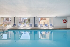 Ein überdachter Swimmingpool mit großen Glaswänden, blauen Liegestühlen und einem Rettungsring an der Wand.
