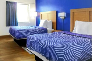 A hotel room with two beds, each with a blue patterned bedspread, a wooden headboard, and a nightstand with a lamp.