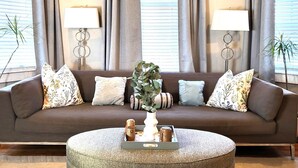 Ein Wohnzimmer mit einem braunen Sofa, zwei Lampen, einem runden Hocker und einem Blumentopf.