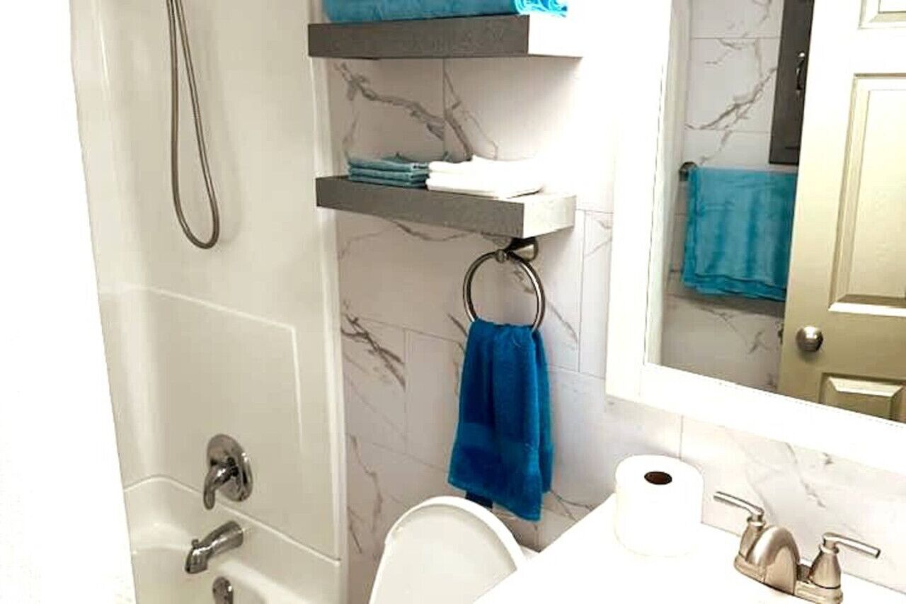 Een badkamer met een bad, toilet, wastafel, spiegel en een handdoekrek met een blauwe handdoek.