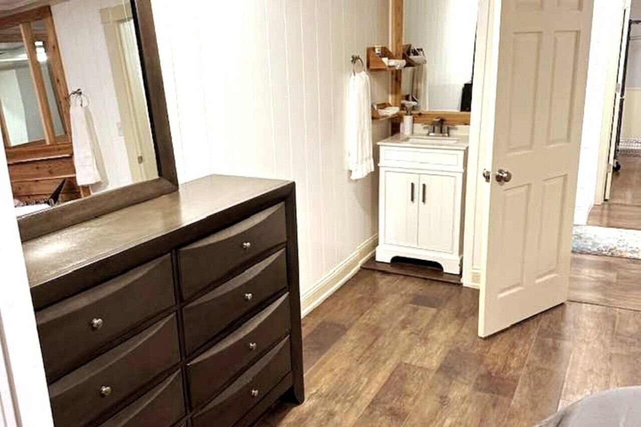Een badkamer met een donkere houten dressoir, witte kasten en een spiegel.