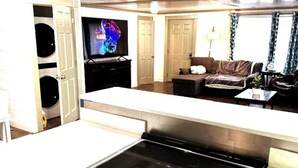 Ett vardagsrum med en platt-TV, en soffa, ett soffbord och en köksdel med en spis.
