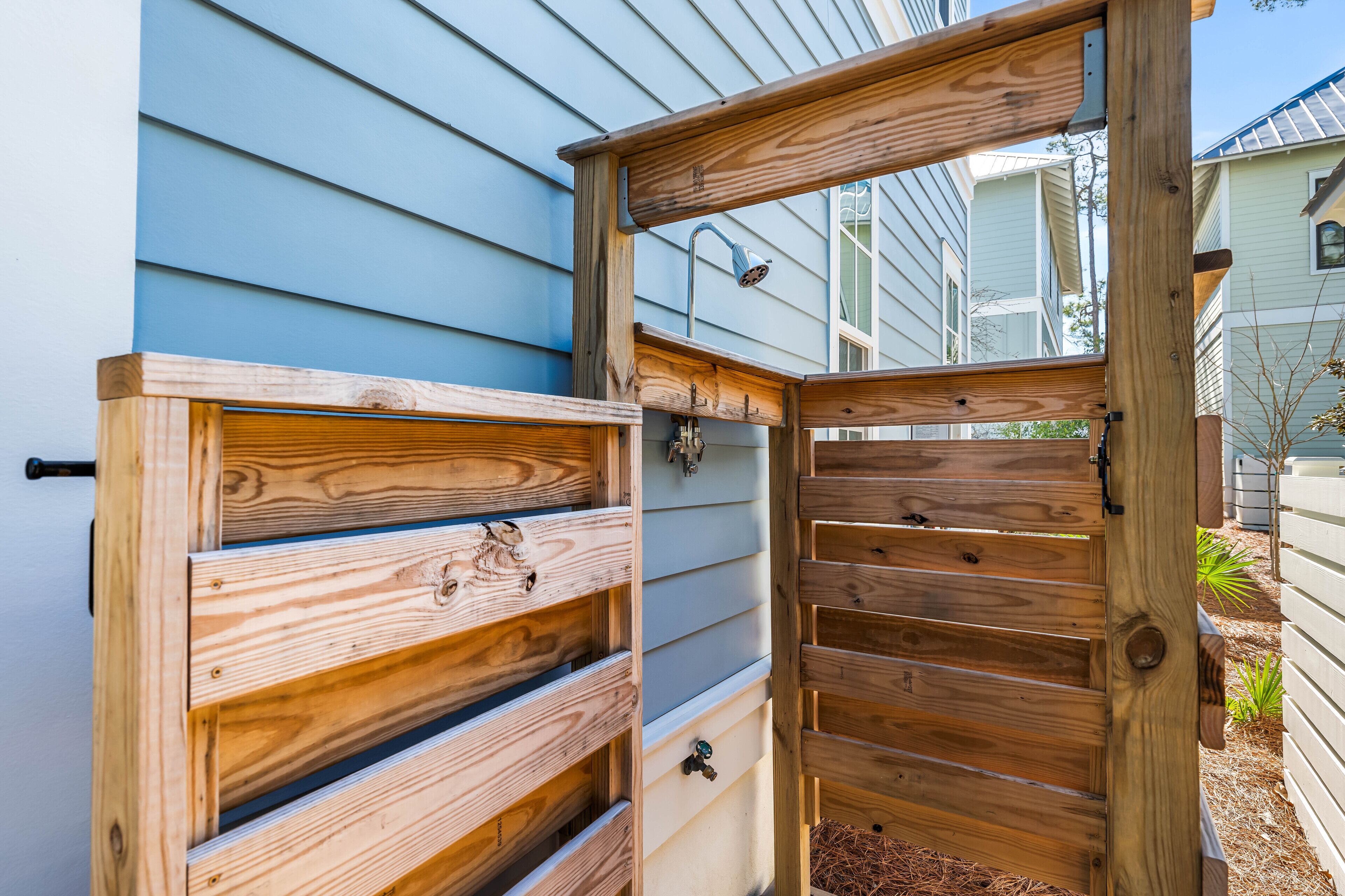A wooden gate with a latch and a metal handle, leading to a covered outdoor area with a metal roof.
