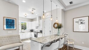 Une cuisine moderne avec des meubles blancs, un îlot en marbre et des luminaires suspendus.