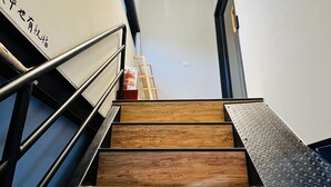 A staircase with wooden steps and metal railings, leading to a landing with a door and a small ladder. - Ocean Tale Inn (Liuqiu)