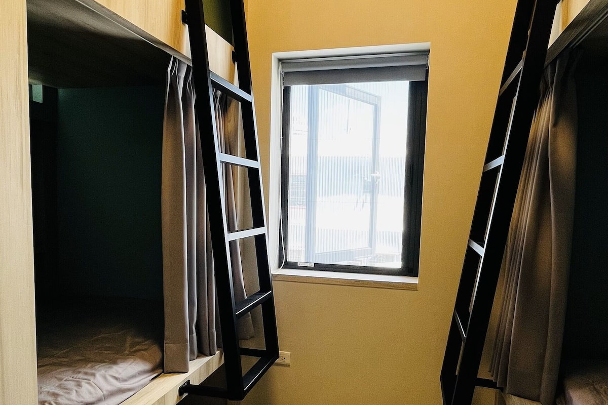A dormitory room with bunk beds, a window, and an air conditioning unit.