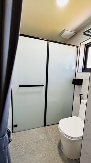A modern bathroom with a glass shower enclosure, a toilet, and a small sink area.