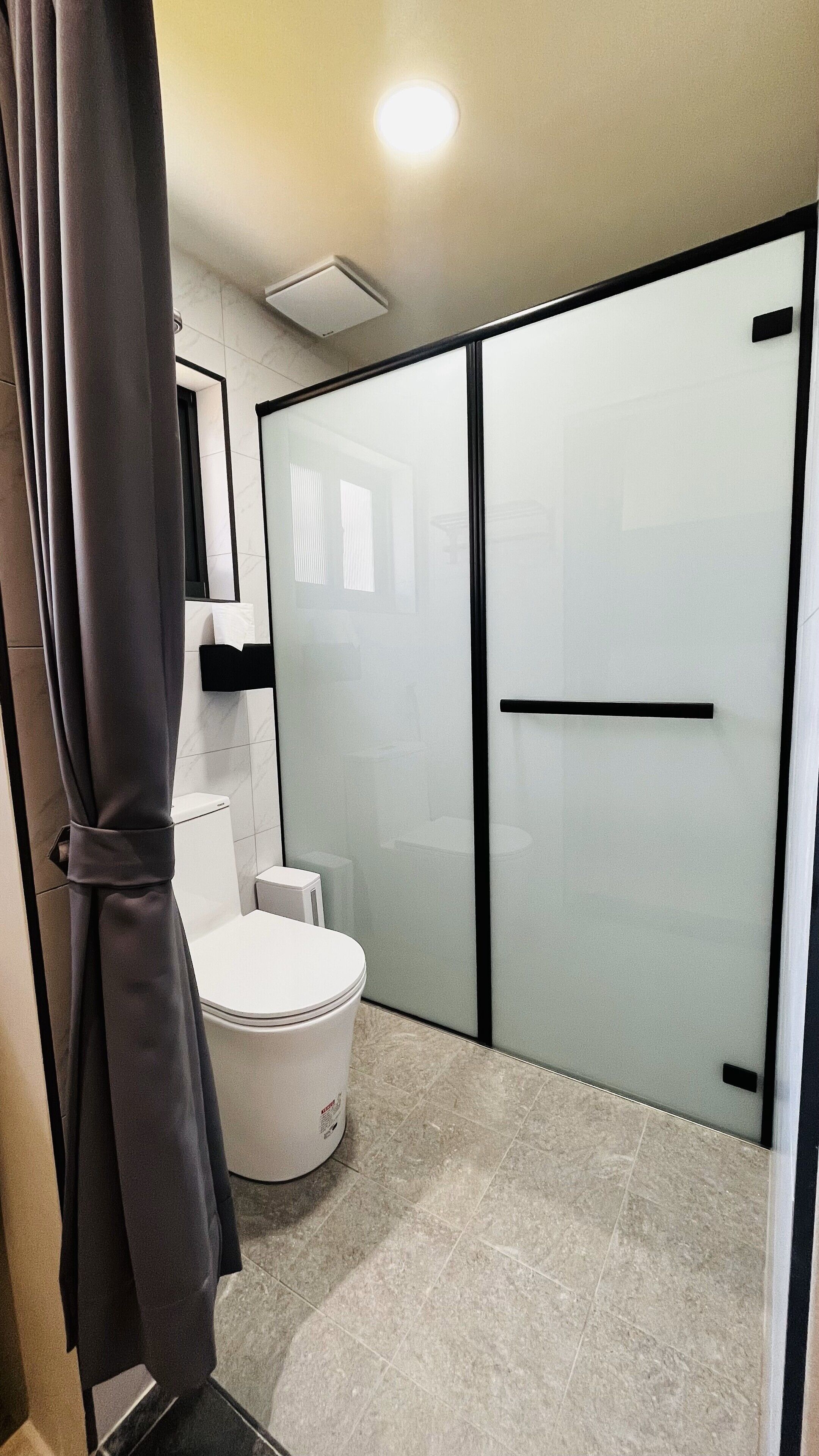 A modern bathroom with a toilet, a shower enclosure, and a glass door.