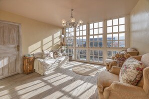 A spacious room with large windows, a chandelier, and a cozy seating area with floral cushions. - A Casa Dos Cregos (Ourense)